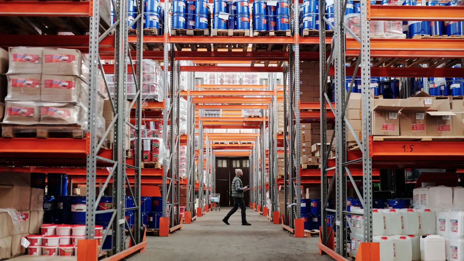 Warehouse worker moving through an aisle of stocked pallet racks during logistics operations