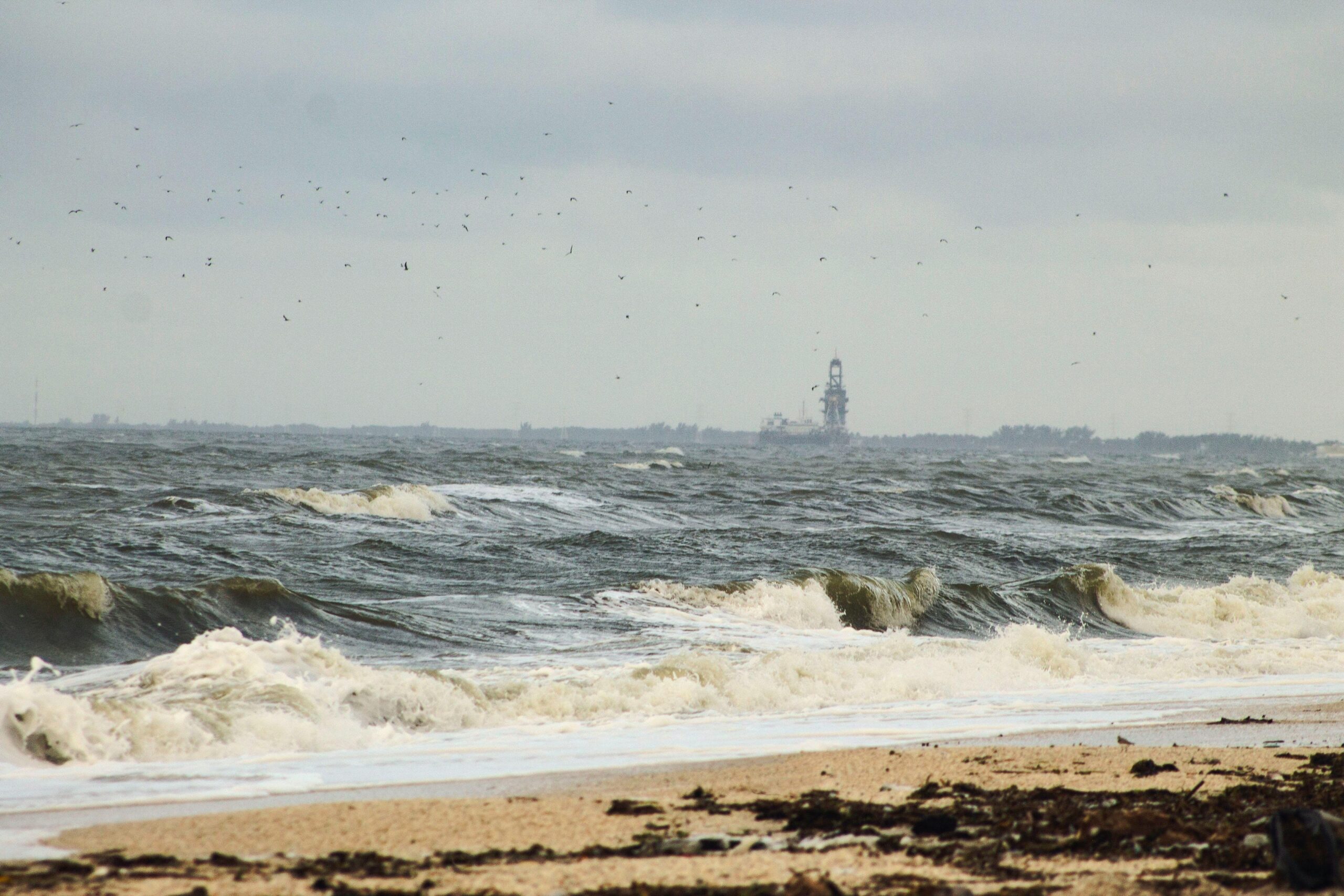Waves crash onto a sandy beach in Ciudad del Carmen, Mexico, with an offshore rig in view.