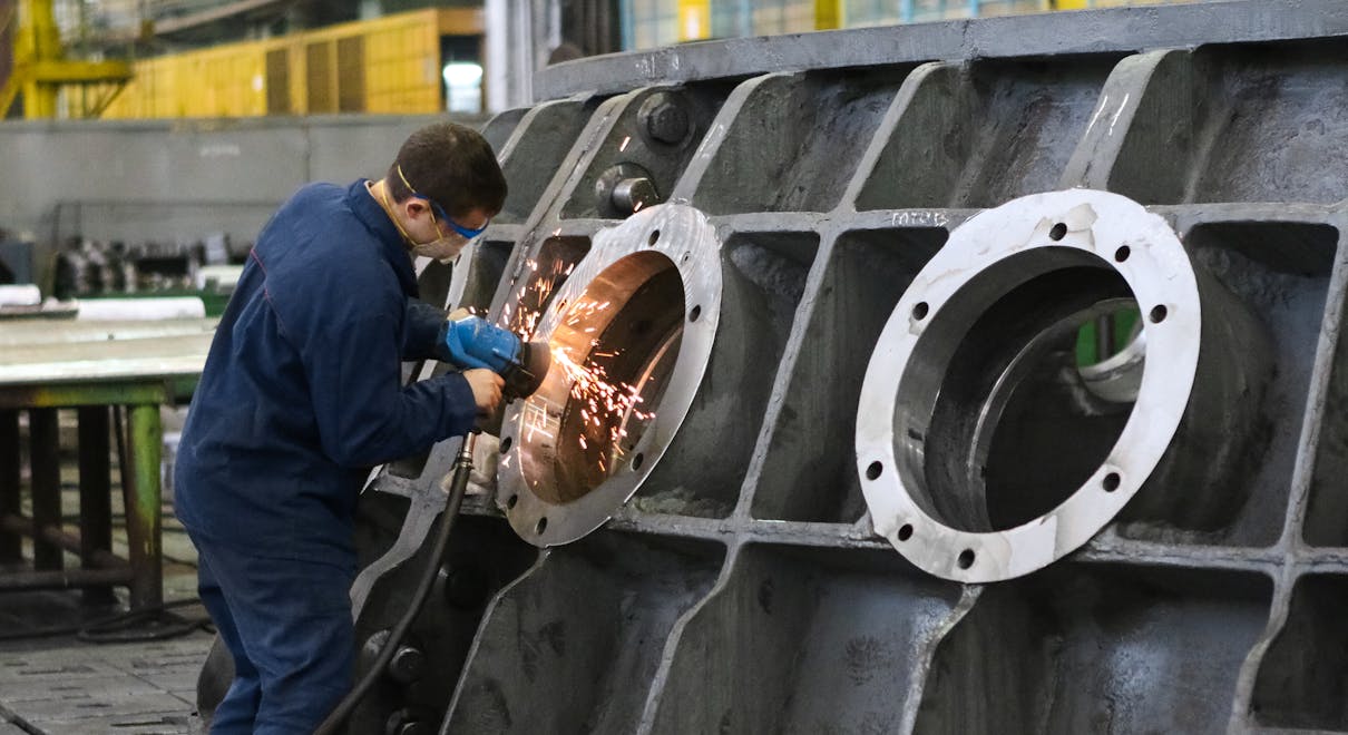 A worker in protective gear grinding metal, creating sparks in a factory setting.