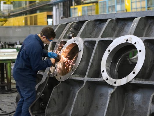 A worker in protective gear grinding metal, creating sparks in a factory setting.