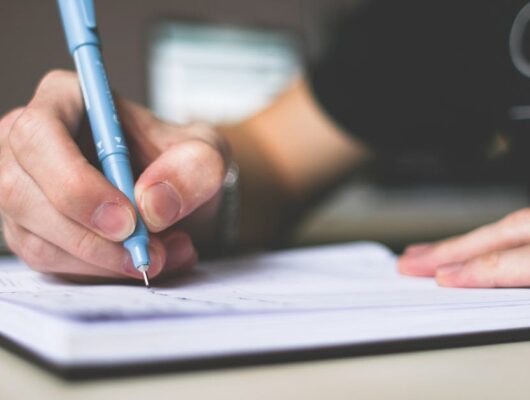 Close-up of hand writing in notebook using a blue pen, focus on creativity.