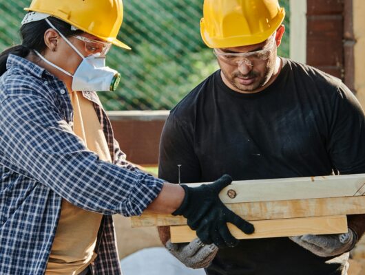 Two construction workers in hard hats collaborating at an outdoor site.