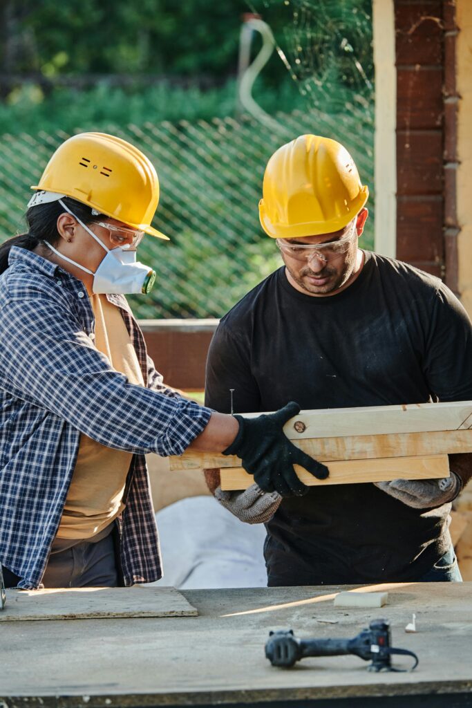 Two construction workers in hard hats collaborating at an outdoor site.