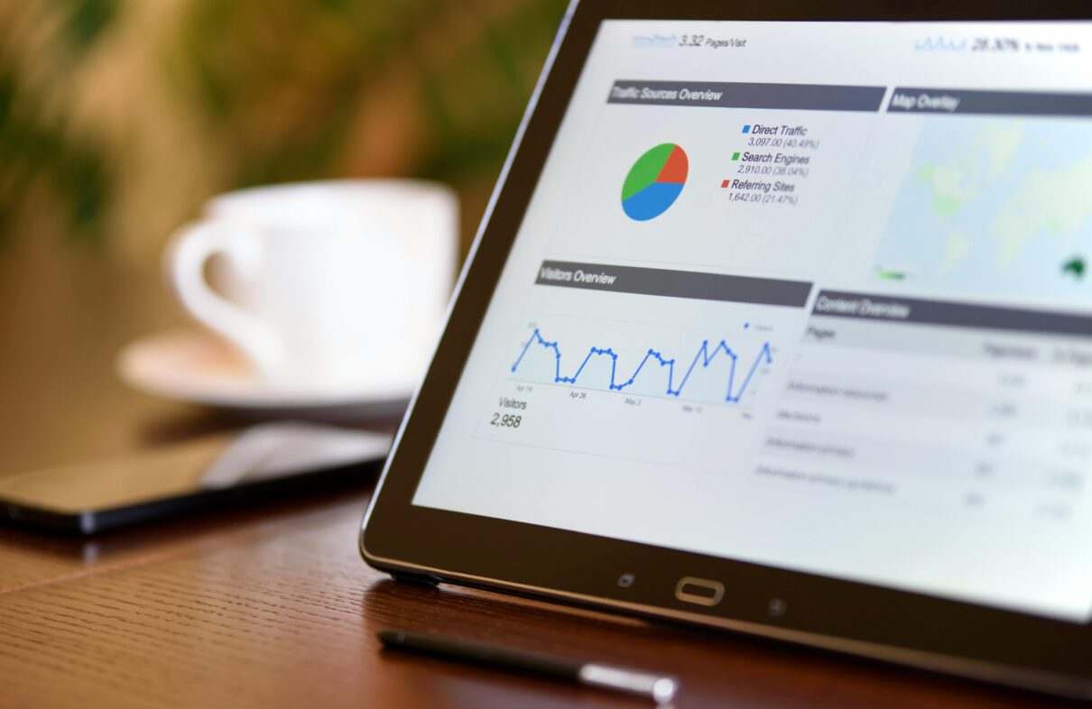 Close-up of a tablet displaying analytics charts on a wooden office desk, alongside a smartphone and coffee cup.
