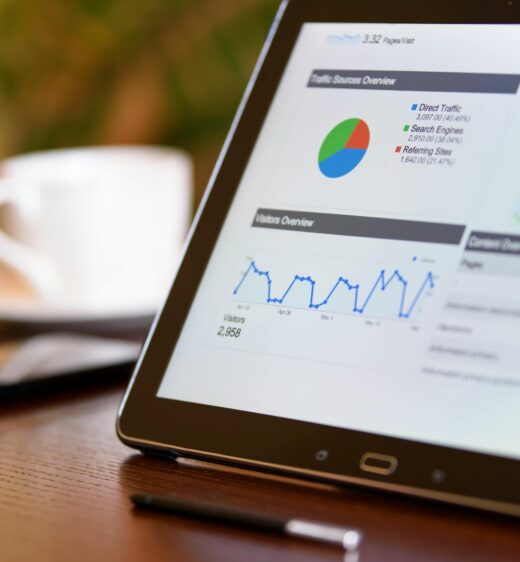 Close-up of a tablet displaying analytics charts on a wooden office desk, alongside a smartphone and coffee cup.