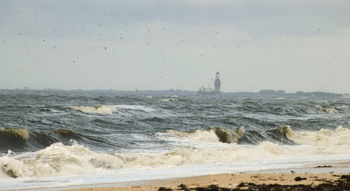 Waves crash onto a sandy beach in Ciudad del Carmen, Mexico, with an offshore rig in view.