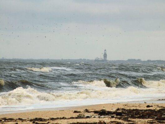 Waves crash onto a sandy beach in Ciudad del Carmen, Mexico, with an offshore rig in view.